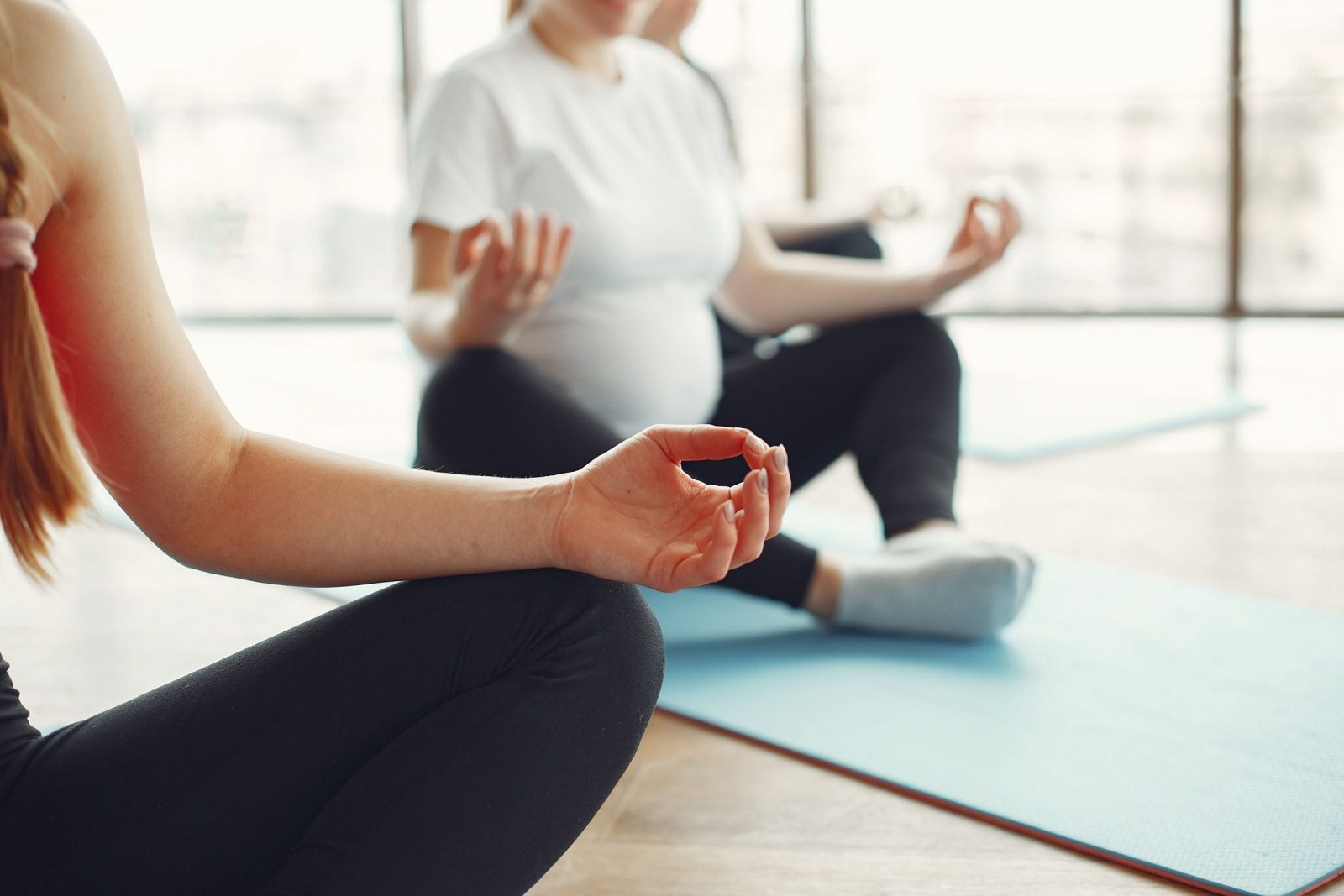 Crop unrecognizable pregnant women sitting on mats and meditating in bound angle pose during yoga class in modern studio of fitness center