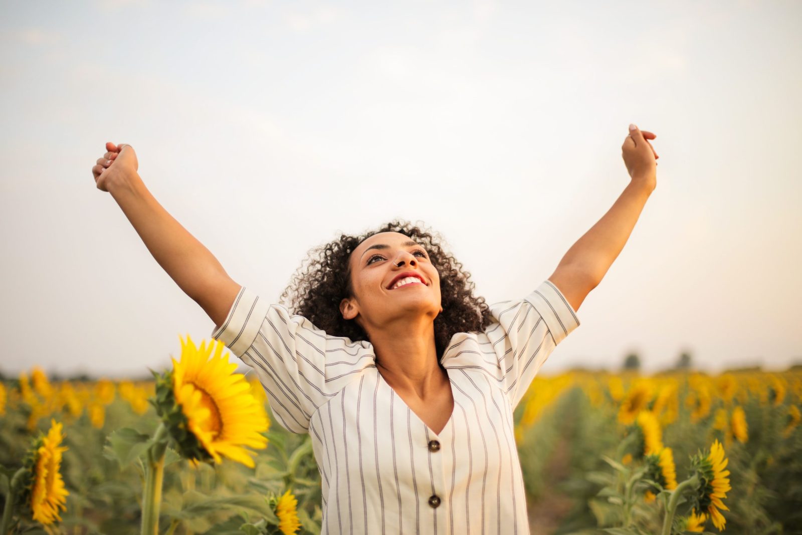 Woman stands in a sunflower field at sunset, exuding joy and freedom.