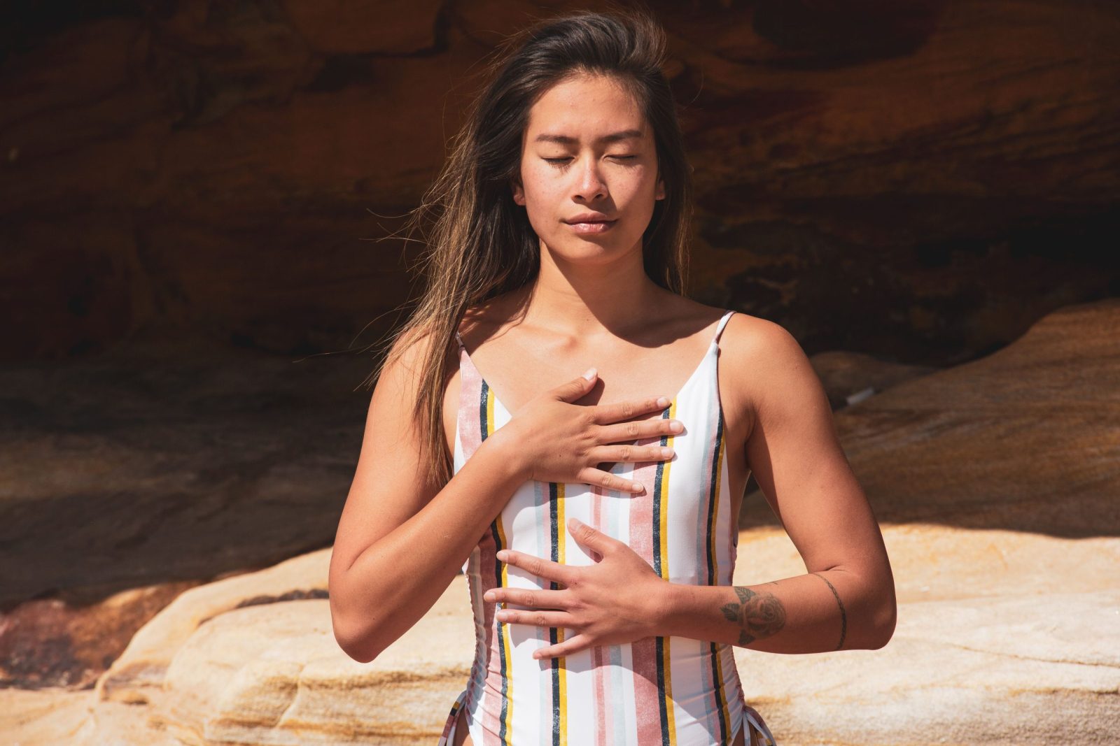 A woman relaxes with chest breathing outdoors, eyes closed in meditative state.