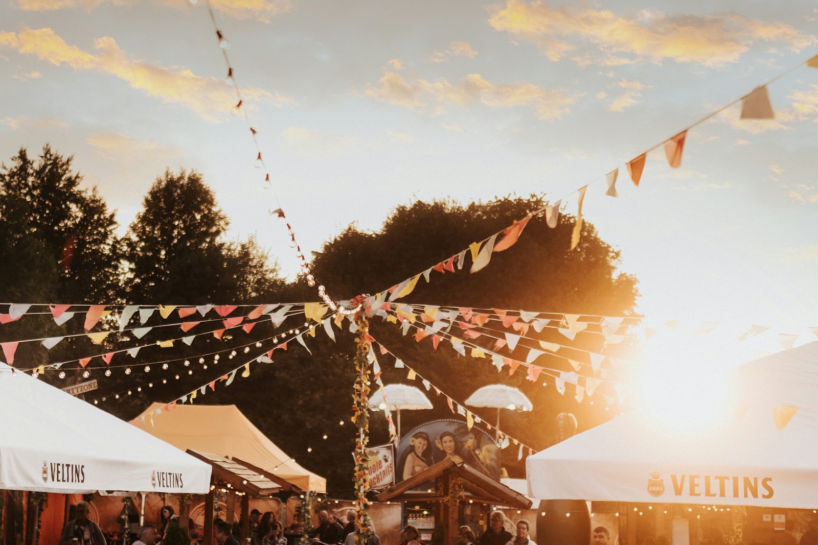 Colorful bunting flags strung above festival stalls under a warm golden sky